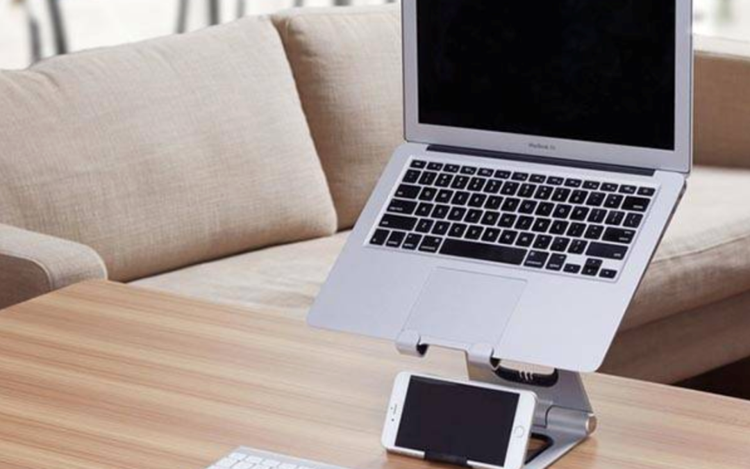 A laptop on a stand above a keyboard, mouse and phone on a desk