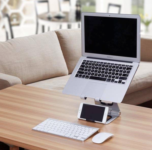 A laptop on a stand above a keyboard, mouse and phone on a desk